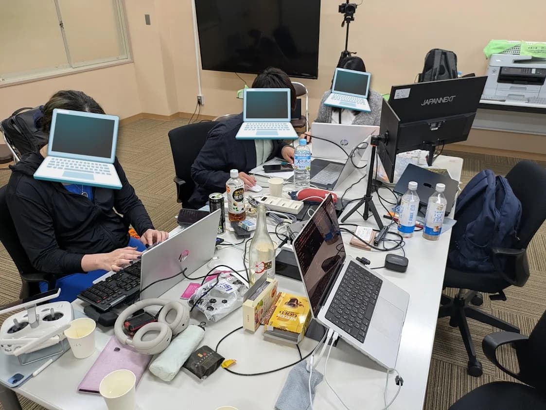 ノートパソコンや機材が並ぶ机で作業するチームDのメンバー
